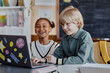 © Seventyfour - Two laughing multiethnic kids engaged in learning on laptop watching funny videos during smart class while sitting at desk