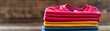 © Media Srock - A stack of colorful shirts on a wooden surface. The shirts are piled on top of each other, creating a colorful and vibrant display. The arrangement of the shirts suggests a sense of organization