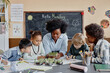 © Seventyfour - Diverse group of students and female teacher over table looking at microgreen sprouts studying growth of plants and learning about environment in classroom