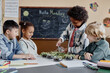 © Seventyfour - Multiethnic group of happy children looking at green plants in glass jars watering microgreen sprouts using spray bottle during biology class at primary school, copy space