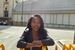 © Connect Images - Smiling woman leaning on a yellow barrier on a sunny city street.