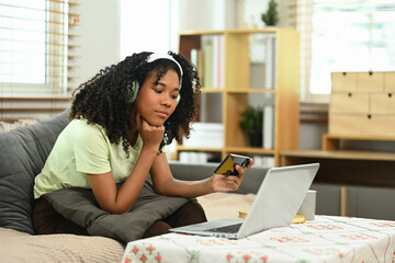 Young African American woman wearing headphone using mobile phone in living room