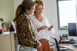 © Connect Images - Two women, one younger and one older, examine a smartphone together in a modern office setting.
