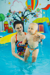 Wall Mural - Swimming pool for children. Little boy in the pool. A baby learns to swim with a coach in the pool. Swimming courses for small children.