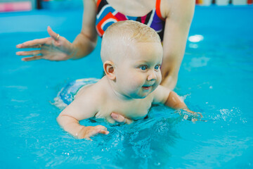 Wall Mural - Little boy in the pool. A baby learns to swim with a coach in the pool. Swimming courses for small children. Swimming pool for children