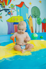 Wall Mural - A baby learns to swim with a coach in the pool. Swimming courses for small children. Baby boy swims in the pool.