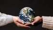 © lililia - Two hands, one pale and one dark-skinned, hold a globe covered in green grass and white continents. The background is a simple gray