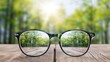 © lililia - A pair of black eyeglasses sit on a wooden surface, reflecting a sunny path through a green forest