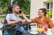 © 24K-Production - Woman helping her husband with a disability to use a mobile phone while they enjoy leisure time at the cafe outdoors.