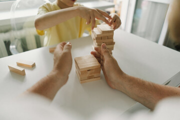 A father and son play a block tower game together indoors. The game is taking place on a white table, and the background is out of focus. Father's day