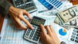 © Plaifah - Close-up of hands counting money with a calculator and financial reports spread out on a desk.