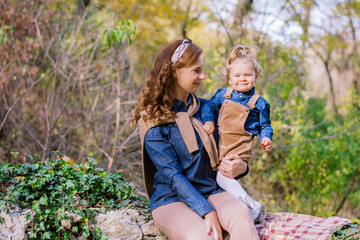 happy mother and her young daughter toddler enjoying day outdoors beautiful autumn forest. mother holding her daughter. smiling looking at the camera. stylish in family look clothes 