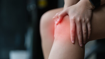 Close up image of female athlete feeling pain and holding her injured knee during exercise at the gym.