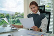 © wattana - Smiling caucasian female executive manager filling paper business document while sitting in modern office.