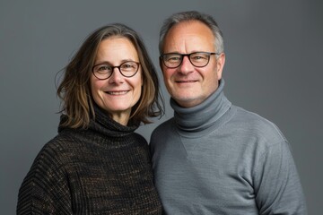 Wall Mural - Portrait of a grinning couple in their 40s wearing a classic turtleneck sweater on blank studio backdrop