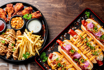 Wall Mural - An appealing arrangement of fast food items including chicken wings, hot dogs, French fries, and sauces on plates.