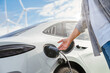 © escapejaja - EV car with electric vihicle charging station, sustainable energy. nature green energy Wind turbines. Sustainability