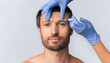 © Prostock-studio - A man receives an injection to his forehead from a doctor wearing blue gloves.