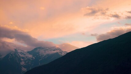 Wall Mural - 4K shot of orange clouds above the snowy Himalayan mountain peak of the Lahaul Valley as seen from Keylong in Himachal Pradesh, India during the sunset. Beautiful dramatic sky during the sunset.