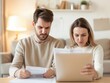 © KanitChurem - A worried couple reviews financial documents at home, displaying stress and concern about their finances in a modern living room setting.