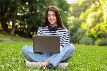 Wall Mural - Smiling freelancer working with laptop on green grass outdoors. Remote job