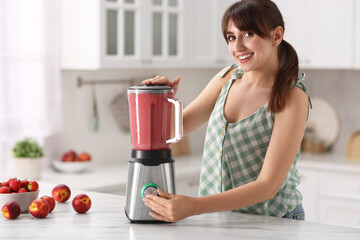 Wall Mural - Young woman making delicious smoothie with blender at white marble table in kitchen