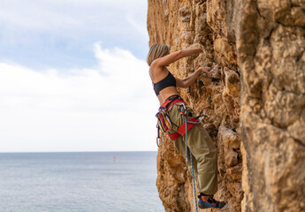 A woman is climbing a rock wall while wearing a black tank top and red