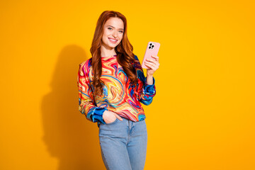 Wall Mural - Photo of adorable positive girl with foxy hair dressed print shirt hold smartphone arm in pocket isolated on yellow color background