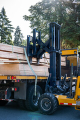 Wall Mural - Forklift unloading a load of lumber from a flatbed delivery truck in a residential neighborhood, sunny summer construction season
