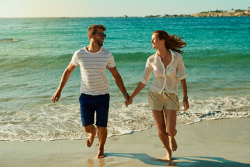 Canvas Print - Happy, couple and holding hands on beach for love, commitment and bonding on summer vacation for honeymoon. Man, woman and together by ocean for romantic holiday, affection and weekend with embrace.