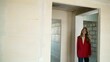 © Ruslan - A cheerful woman walks through a modern apartment, enters a new house, a happy young woman stands in the doorway of the apartment. The woman is happy with her new apartment without renovation. A young
