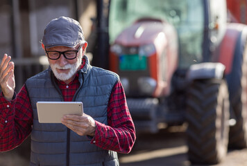 Wall Mural - Farmer looking at tablet in front of tractor on cow farm