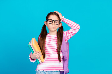 Canvas Print - Photo of upset girl dressed striped shirt backpack on shoulder in glasses hold book palm on head isolated on blue color background