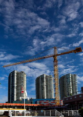 Wall Mural - Construction of new building in residential area   in New Westminster city, construction crane and three skyscrapers on the background of blue cloudy sky