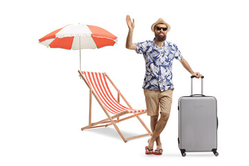 Wall Mural - Full length portrait of a bearded man with a suitcase next to a beach chair waving at camera