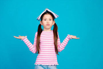 Poster - Photo of small girl dressed striped shirt holding book on head arms comparing products empty space isolated on blue color background