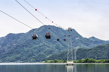 Chuncheon-si, Gangwon-do, South Korea - May 24, 2023: Low angle view of cable cars driving on Uiam Lake against Samaksan Mountain in summer
