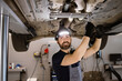 © sofiko14 - Mechanic smiling while wearing headlamp and repairing car in auto repair shop. Person ensures vehicle maintenance and safety while working in professional environment.
