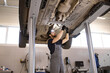 © sofiko14 - Mechanic inspecting and repairing vehicle on lift in auto repair shop. Professional technician performing maintenance and diagnostics under car. Industrial environment highlighting car service.