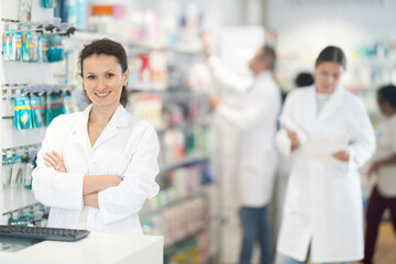 Wall Mural - Positive middle-aged female pharmacist standing at the desk using keyboard in chemist's shop