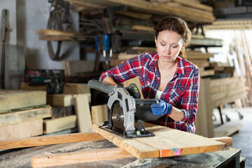 Wall Mural - Woman employee performs cutting of wooden board using circular stationary saw. Cutting board into pieces with specified parameters in carpentry workshop