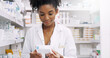 © peopleimages.com - Woman, pharmacist and checking box with medication, side effects or symptoms at pharmacy. Young African, female person or medical employee reading expiry date on pharmaceutical product at store
