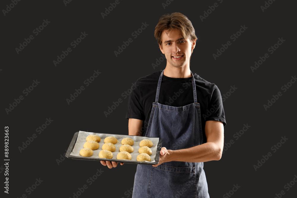 Handsome young man with tray of fresh raw buns on black background