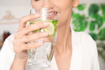 Sticker - Young woman with glass of cucumber water at home, closeup