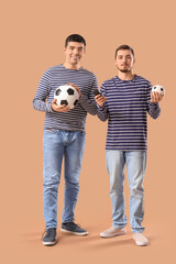 Wall Mural - Handsome young brothers with football balls on beige background