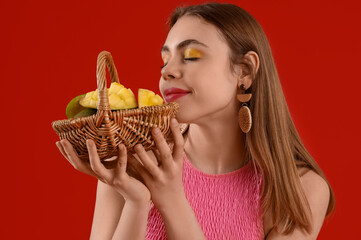 Beautiful young woman holding wicker basket with sweet mango fruits on red background