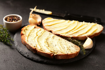 Wall Mural - Board of bread slices with fresh butter, garlic and peppercorn on black background