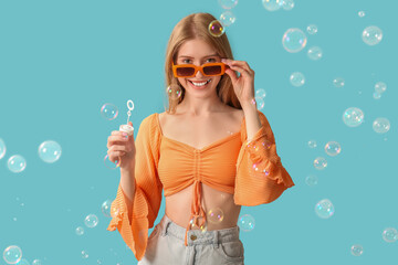 Canvas Print - Happy young woman in sunglasses with soap bubbles on blue background