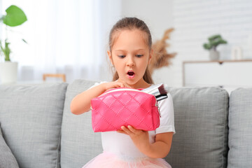 Sticker - Cute little girl with cosmetic bag sitting on sofa in living room