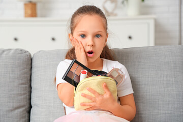 Sticker - Shocked little girl with cosmetic bag sitting on sofa in living room